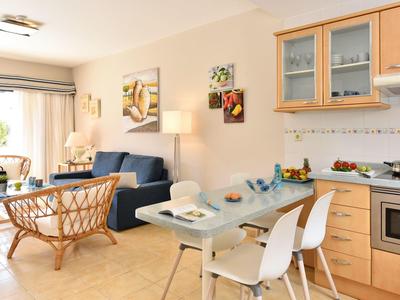 Salle à manger et salon lumineux avec table à manger, canapé, chaises en rotin et cuisine.