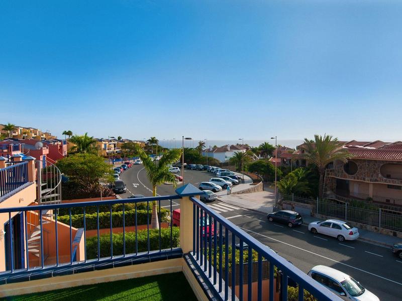 Vue depuis un balcon sur un parking et une rue par une journée ensoleillée dans un quartier résidentiel.