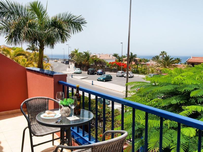 Balcon avec table, chaises et vue sur palmier dans un cadre hôtelier ensoleillé.