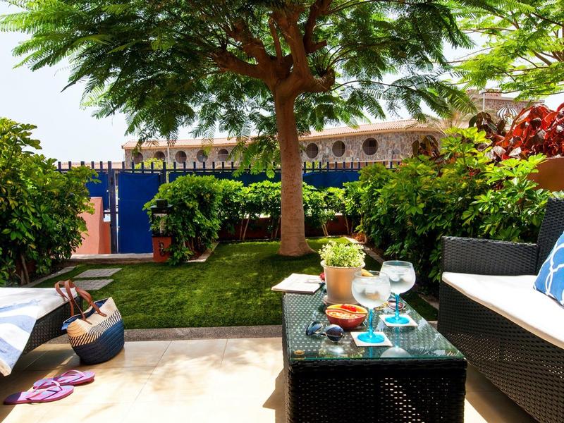 Terrasse confortable avec canapé, table et vue sur un jardin luxuriant et une piscine.