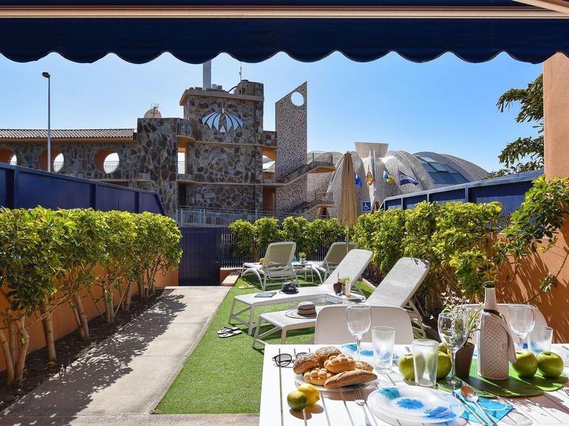 Terrasse confortable avec chaises longues, table dressée et vue sur des bâtiments modernes.
