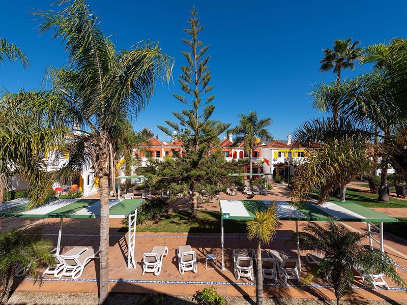 Residencia vacacional con palmeras y mobiliario de jardín bajo un cielo claro.