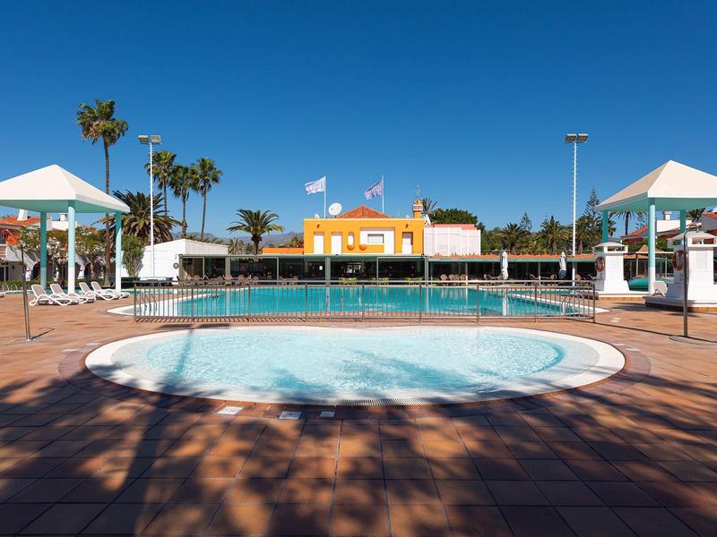 Área de piscina con dos jacuzzis y piscina vacía bajo cielo azul, palmeras al fondo.