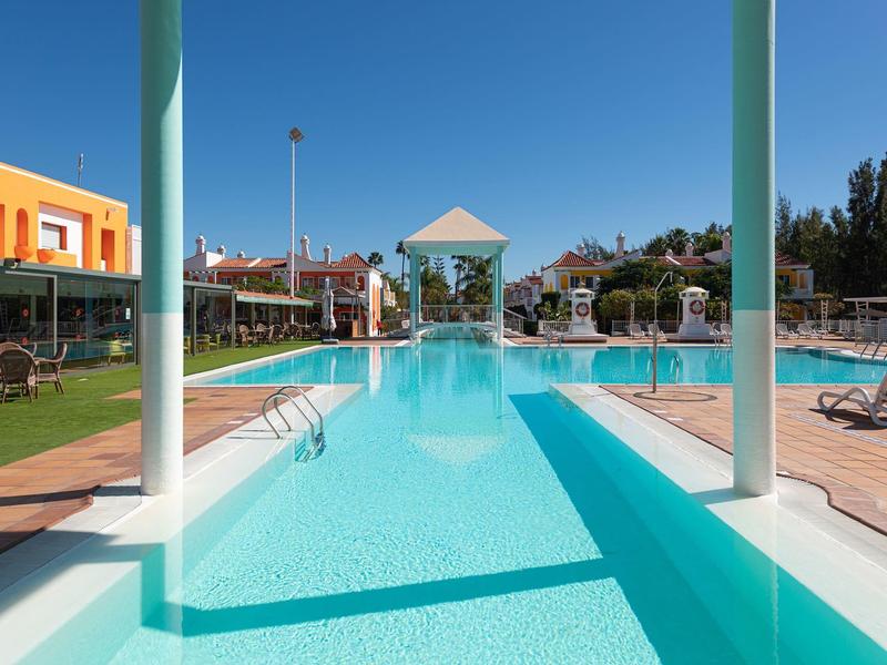 Piscina exterior moderna con agua azul clara y tumbonas bajo cielo azul en zona hotelera.
