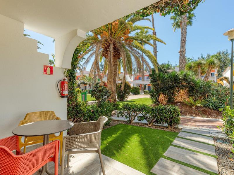 Terraza con sillas y mesa con vista a jardín con palmeras y camino en área del hotel.