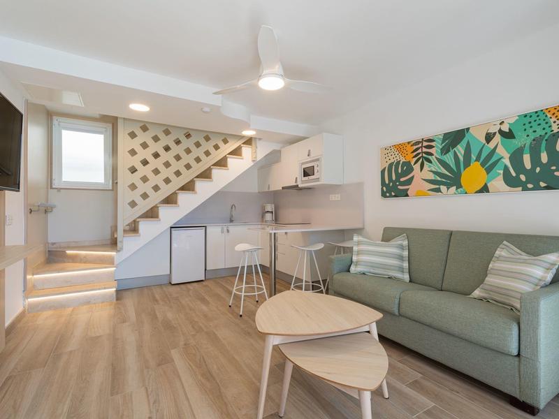 Sala de estar moderna con sofá, mesas de centro y escalera de madera clara en un apartamento vacacional.