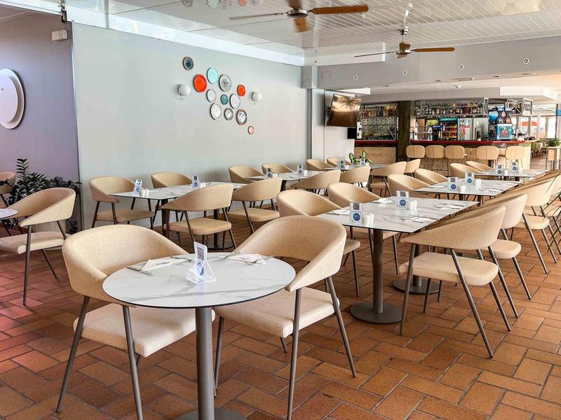 Cafetería luminosa con sillas y mesas modernas sobre suelo de terracota, decoración de círculos de colores en la pared.