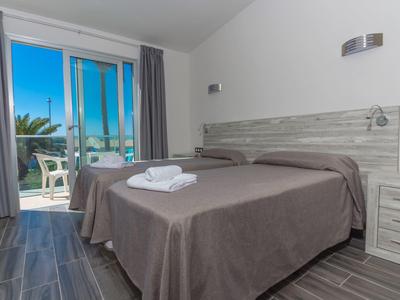 Camera d'hotel moderna con due letti singoli e balcone con vista su palme.