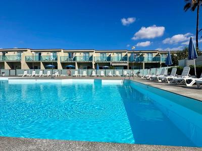 Acqua limpida nella piscina dell'hotel con lettini e cielo azzurro sullo sfondo.