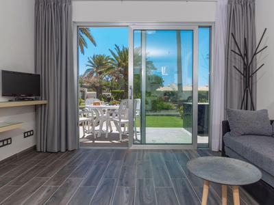 Area soggiorno moderna con porta scorrevole in vetro verso il balcone e vista su palme e terrazza.