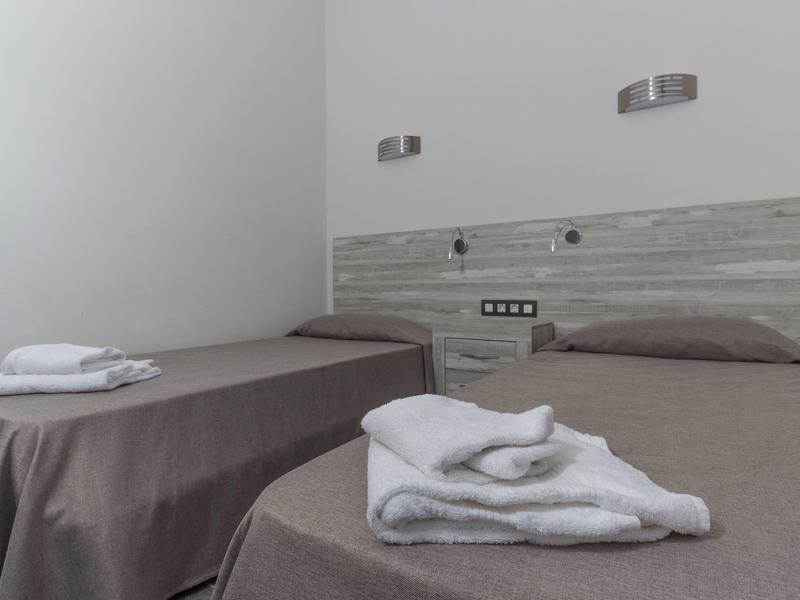 Camera d'hotel semplice con due letti singoli, coperte marroni e asciugamani sopra.