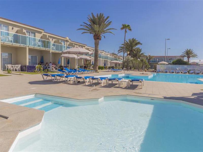 Grande piscina dell'hotel con lettini e palme sotto un cielo azzurro limpido.