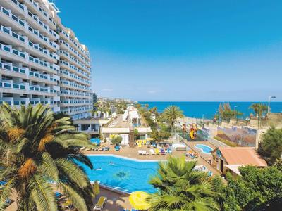 Großes Hotel neben Palmen, Pool und Meer unter klarem blauem Himmel.