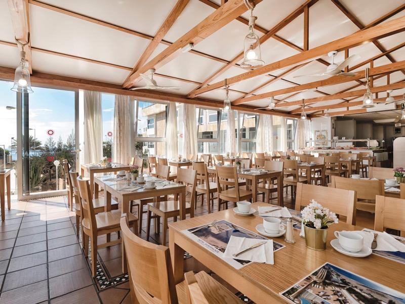 Ristorante luminoso con arredi in legno, tavoli apparecchiati e ampie finestre panoramiche con vista.