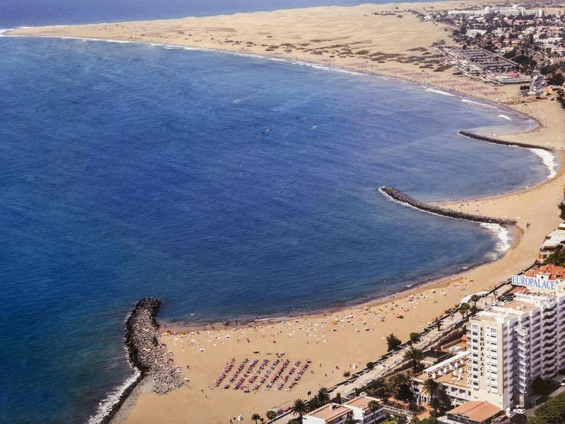 Spiaggia con sabbia dorata, frangiflutti e un hotel lungo la costa.