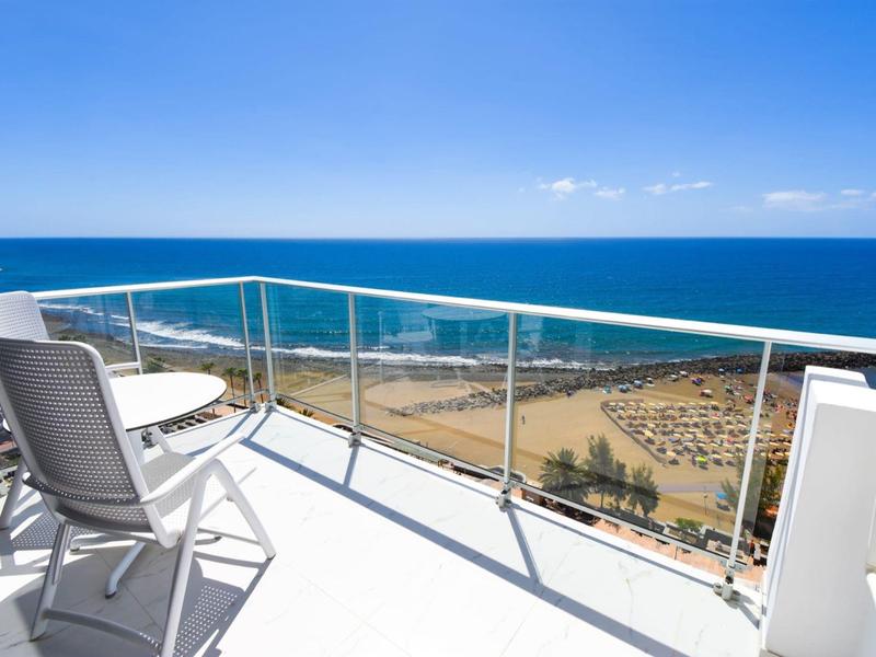 Balcone con due sedie e un tavolo con vista sul mare in una giornata di sole.