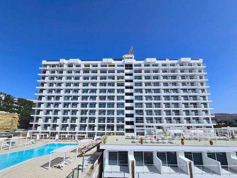 Grande edificio bianco dell'hotel con molti balconi e una piscina davanti sotto un cielo sereno.