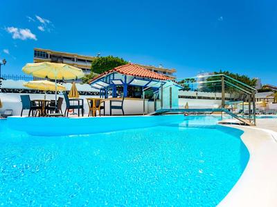 Ein klarer blauer Pool mit Sonnenschirmen und Sitzgelegenheiten unter blauem Himmel.