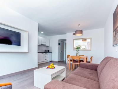 Soggiorno luminoso con divano marrone, tavolo da pranzo, TV e cucina moderna sullo sfondo.