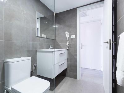 Bagno moderno in hotel con WC, lavabo, specchio e pareti e pavimento piastrellati grigi.