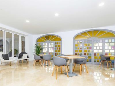 Ampia area lounge dell'hotel con sedie moderne, tavoli rotondi e grande finestra con vetri colorati.