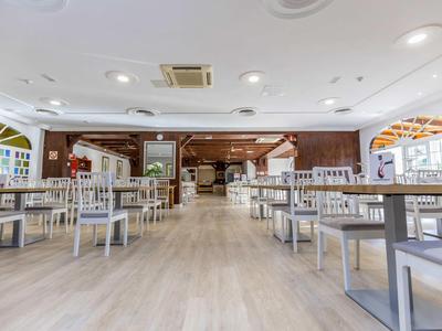 Ampia e luminosa sala da pranzo con sedie bianche e tavoli in legno in un hotel.