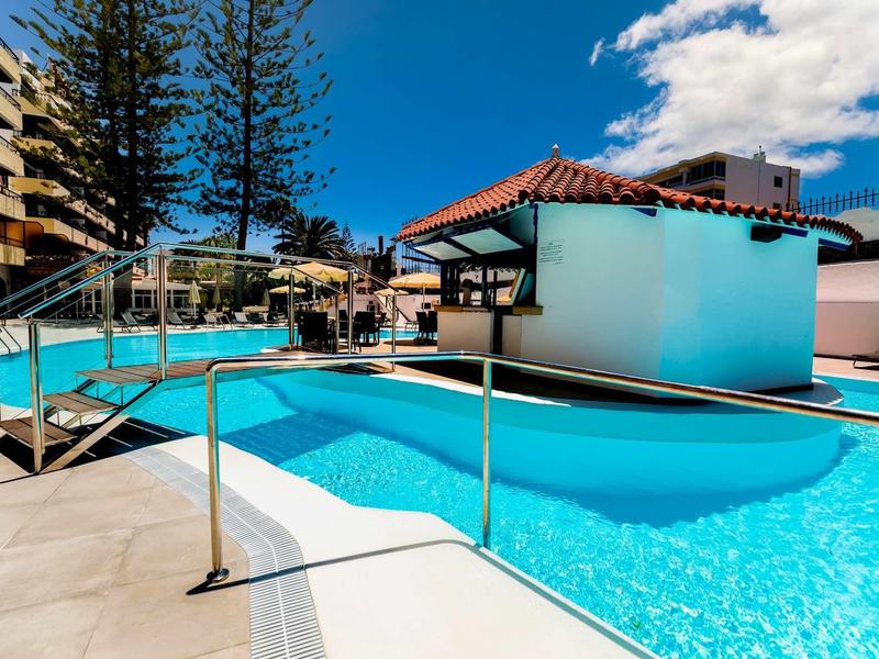Piscina limpida con corrimano accanto a edifici bianchi e cielo blu.