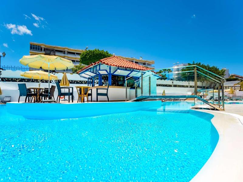 Piscina con acqua limpida, ombrelloni e aree salotto sotto un cielo blu.