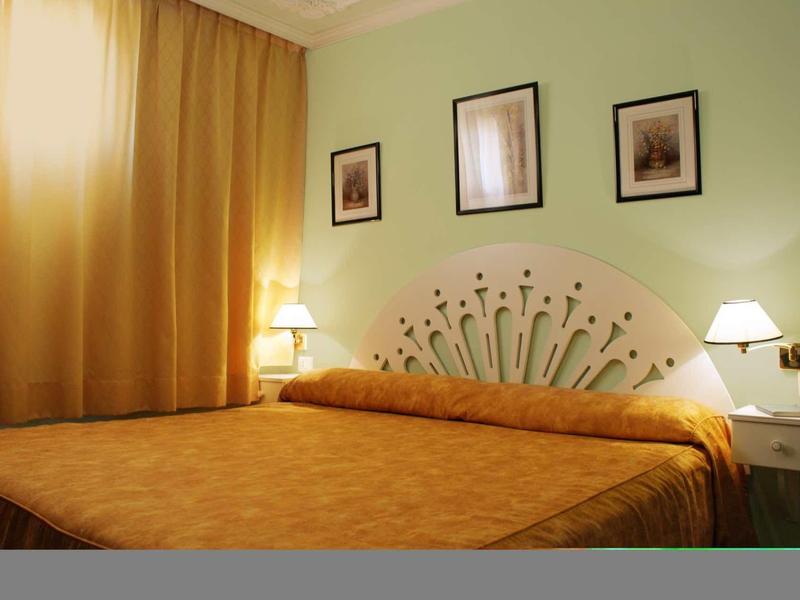 Camera d'hotel accogliente con letto grande, tende gialle e pareti verdi.