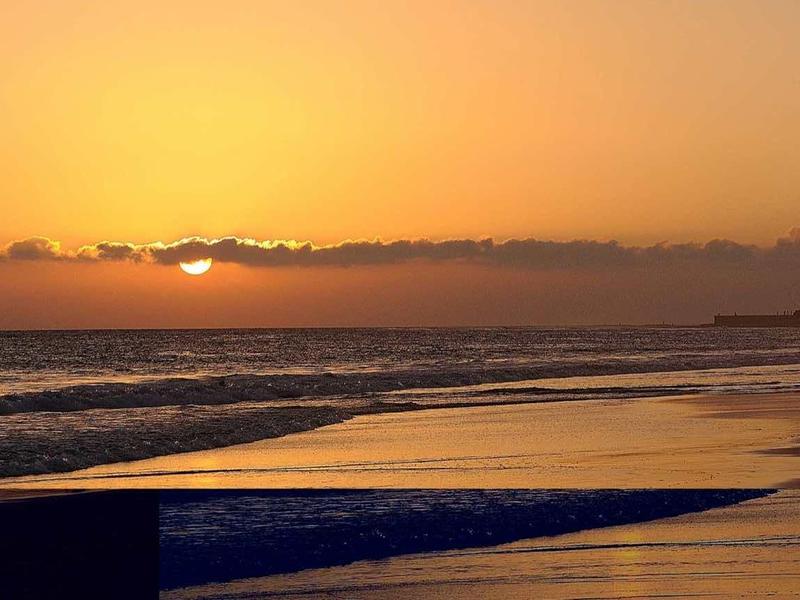 Tramonto sulla spiaggia con faro e mare calmo