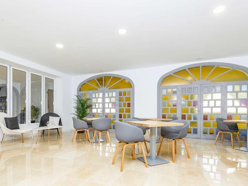 Ampia area lounge dell'hotel con sedie moderne, tavoli rotondi e grande finestra con vetri colorati.