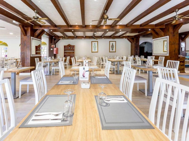 Ristorante luminoso con soffitto a travi in legno e sedie bianche attorno a tavoli in legno