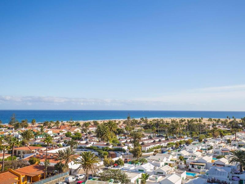Vista di una città costiera con case, palme e mare sotto un cielo azzurro e limpido.