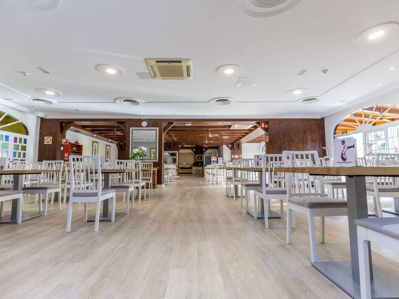 Ampia e luminosa sala da pranzo con sedie bianche e tavoli in legno in un hotel.