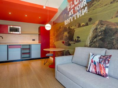 Modern eingerichtetes Hotelzimmer mit Küchenzeile, roter Wand und grauem Sofa.