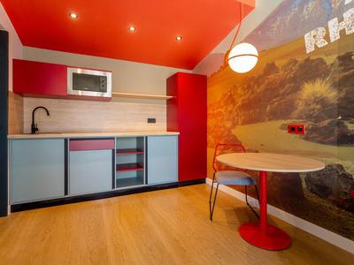 Piccola cucina moderna con accenti rossi e pavimento in legno chiaro in una camera d'hotel.