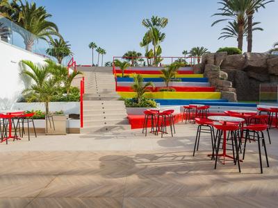 Scale esterne colorate con posti a sedere e palme sotto un cielo sereno.