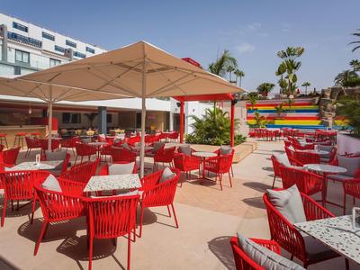 Terrazza dell'hotel con sedie rosse e tavoli sotto ombrelloni in una giornata serena.