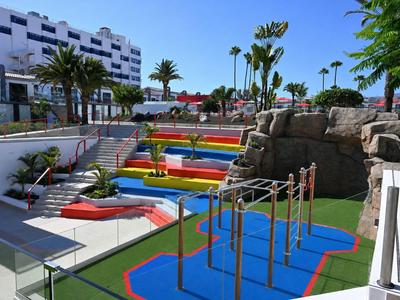 Bunter Outdoor-Fitnessbereich mit Treppen und Palmen vor einem Hotelgebäude.