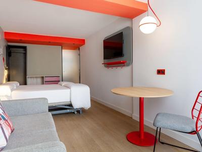 Camera d'hotel moderna con letto matrimoniale, divano, tavolo rotondo e TV a parete.