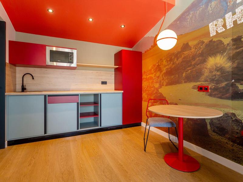 Piccola cucina moderna con accenti rossi e pavimento in legno chiaro in una camera d'hotel.