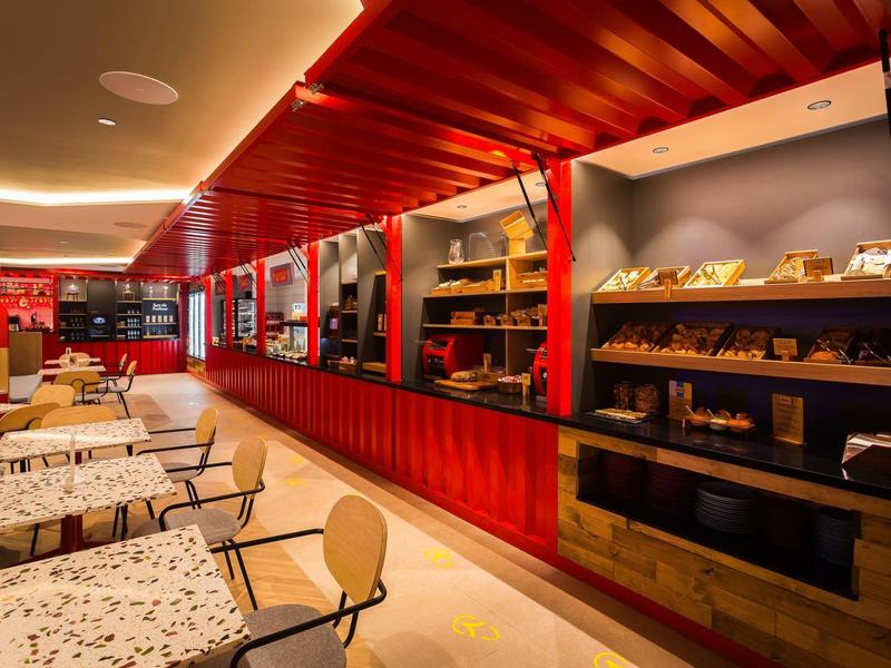 Interno di panetteria d'hotel ben illuminato con pareti rosse e tavoli con sedie.