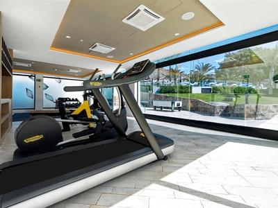 Moderne Fitnessgeräte in einem hellen Fitnessraum mit großen Fenstern und Blick auf Außenbereich.