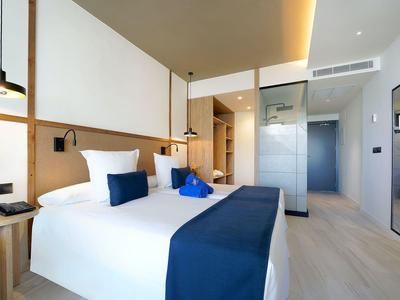 Jasny pokój hotelowy z dużym łóżkiem, niebiesko-białą pościelą i nowoczesnym drewnianym wystrojem.