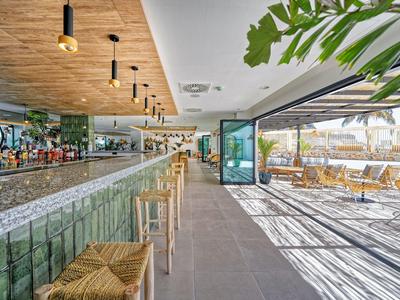 Nowoczesny bar hotelowy z detalami z drewna i szkła, jasną podłogą i przytulnymi miejscami na zewnątrz.