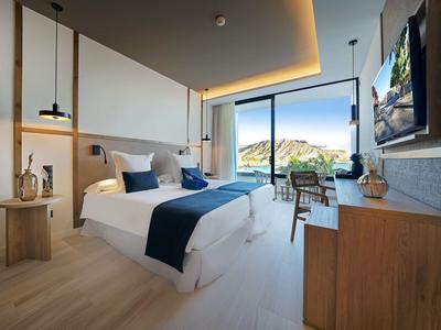 Nowoczesny pokój hotelowy z dużym łóżkiem, biurkiem i panoramicznym oknem z widokiem na góry.