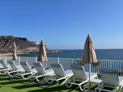 Rzędy leżaków i parasoli na tarasie z widokiem na morze i górę.
