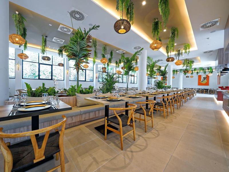 Nowoczesna restauracja z drewnianymi stołami, krzesłami i bujną zielenią w jasnej atmosferze.