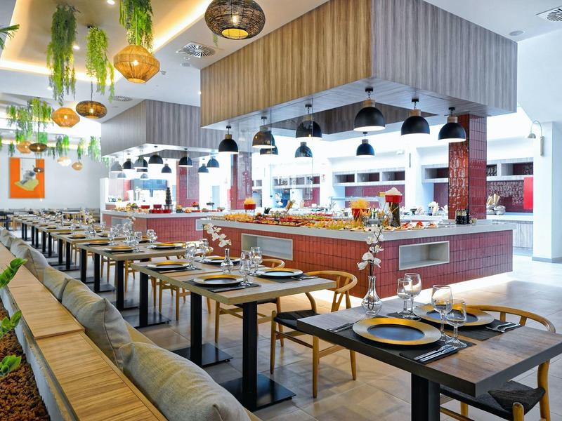 Nowoczesna restauracja z nakrytymi stolikami, drewnianymi meblami, wiszącymi roślinami i lampami.