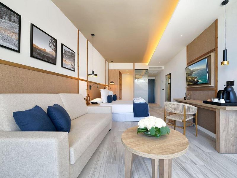 Jasny pokój hotelowy z sofą, podwójnym łóżkiem, biurkiem i nowoczesnym wystrojem.